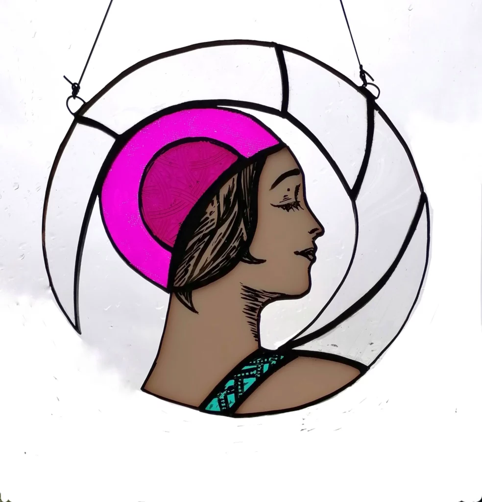 Image shows a Hanging Stained Glass Artwork of a woman in a green swimsuit with a pink swimming cap by local artist Charlotte Savil